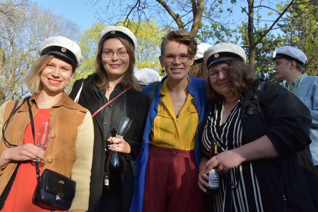 Fyra personer, tre av dem klädda i studentmössa, står och håller om varandra i en park.