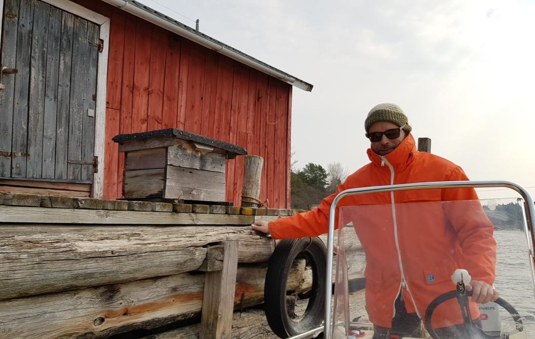 Man i båt intill en brygga. På bryggan finns en postlåda dit han levererar post.