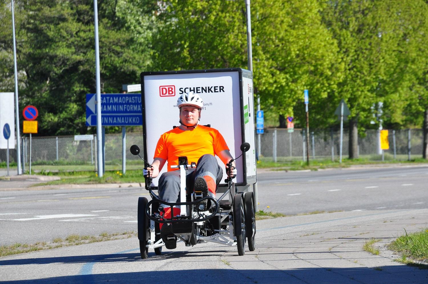 En person sitter på en stor elcykel med fyra hjul och en låda bakom.