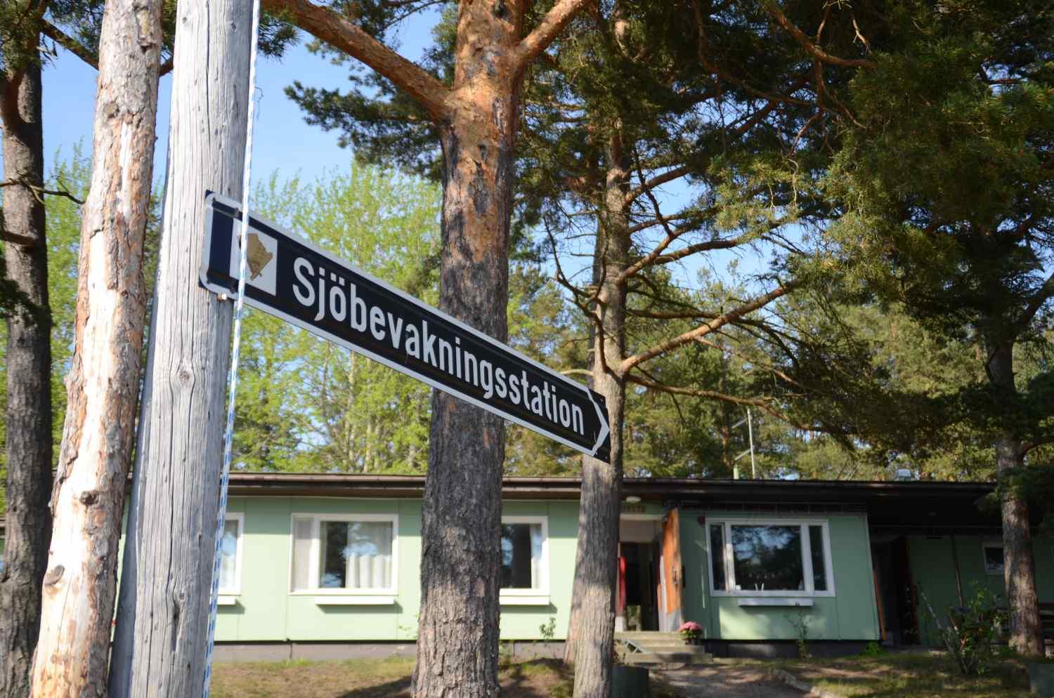 Skylt med texten sjöbevakningsstation på och et hus i bakgrunden.