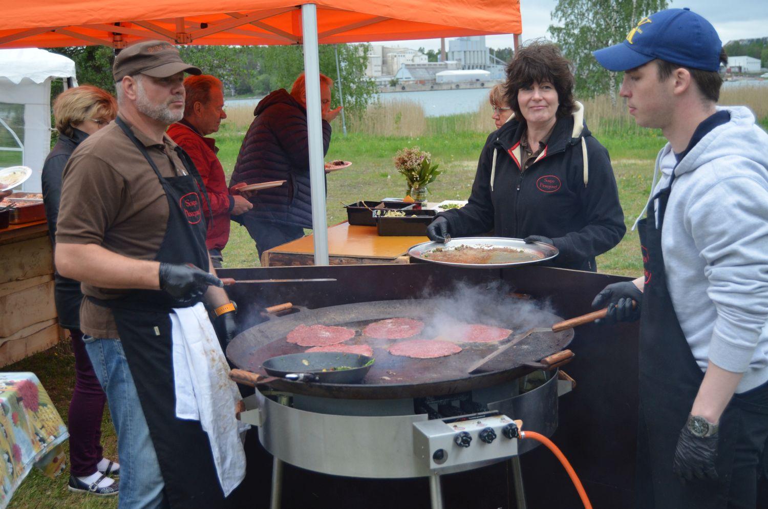Människor steker stora biffar utomhus