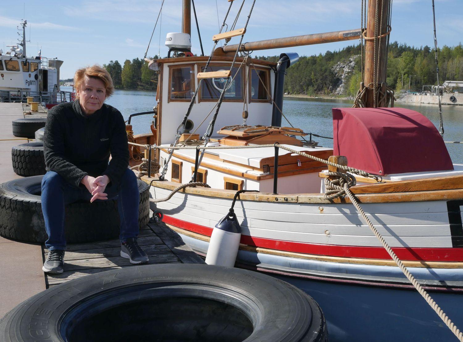 Kvinna sitter på brygga med båtar i bakgrunden