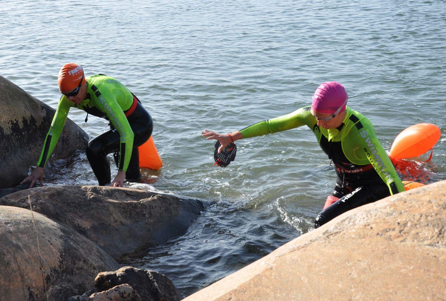 Två kvinnor klättar upp ur havet på strandklippa