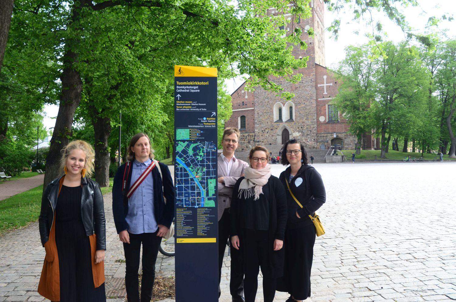 En del av arbetsgruppen bakom projektet står invid den nya skylten vid Domkyrkotorget.