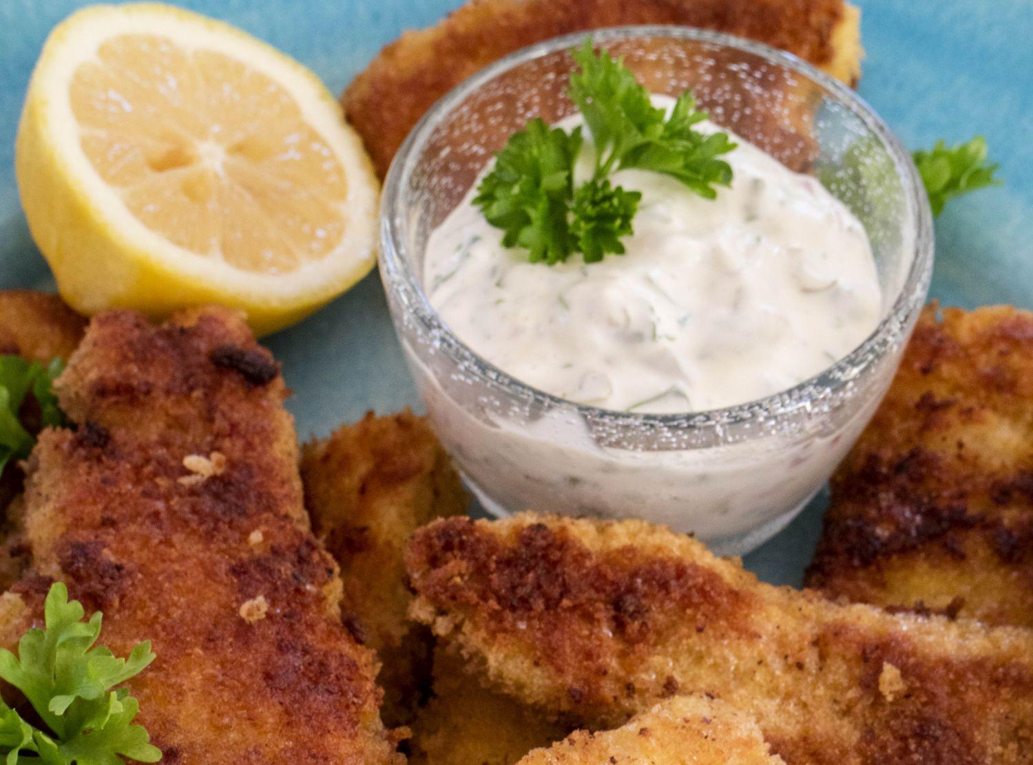Fiskpinnar, en skål med sås och en citron.