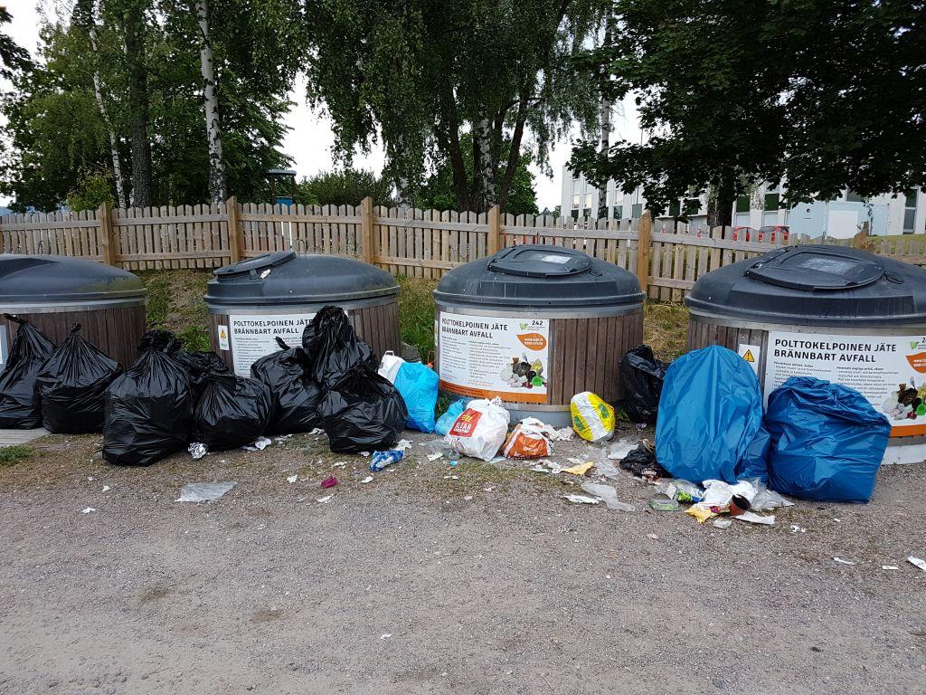 Sopsorteringskärl, framför dem sopsäckar och annat skräp som lämnats.