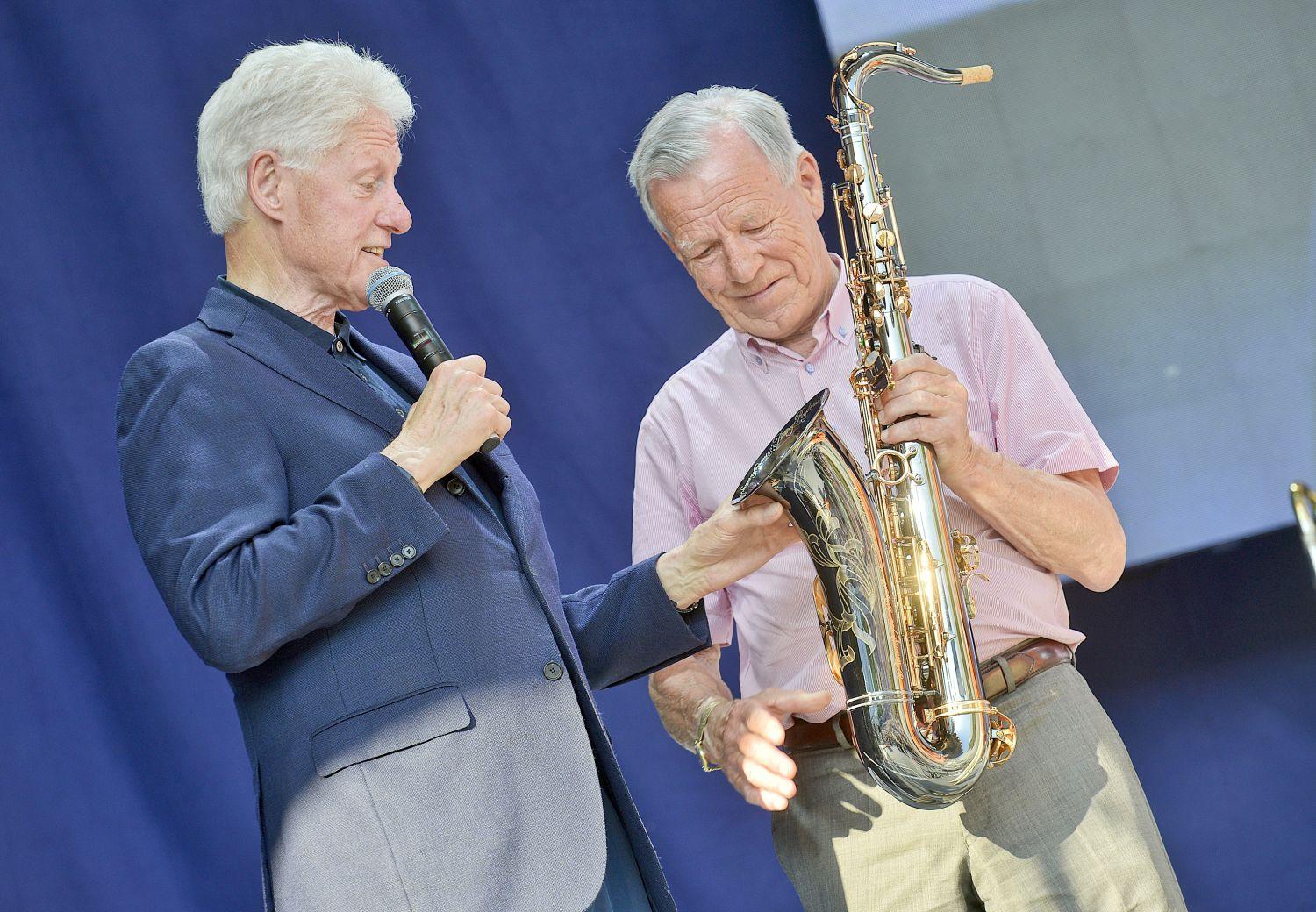 Bill Clinton och Anders Wiklöf står på en scen. Wiklöf överräcker en saxofon till Clinton.