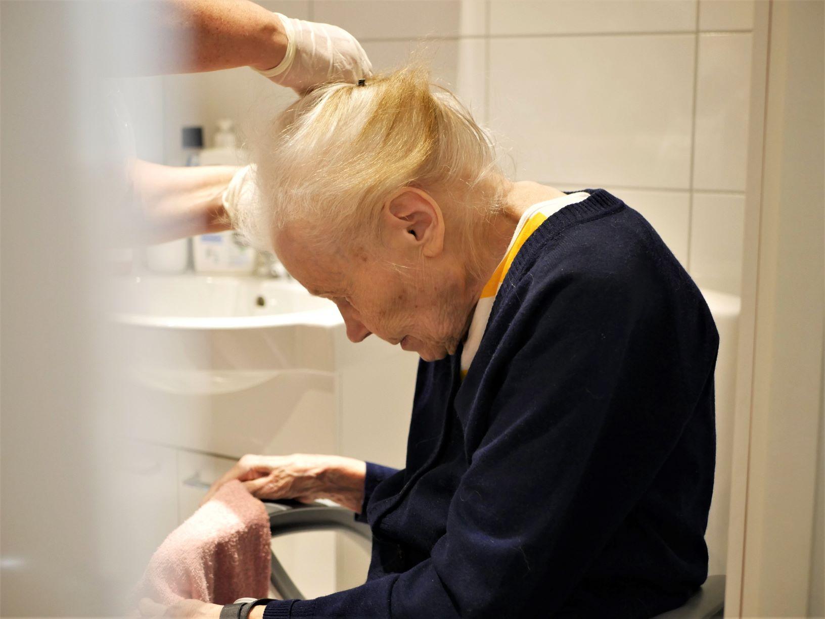 äldre kvinna får håret uppsatt.
