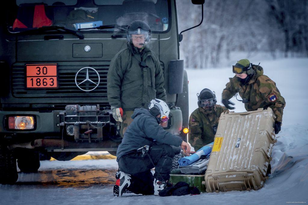 Fyra personer klädda i varma kläder samlas kring någon form av utrustning. I bakgrunden syns en lastbil.