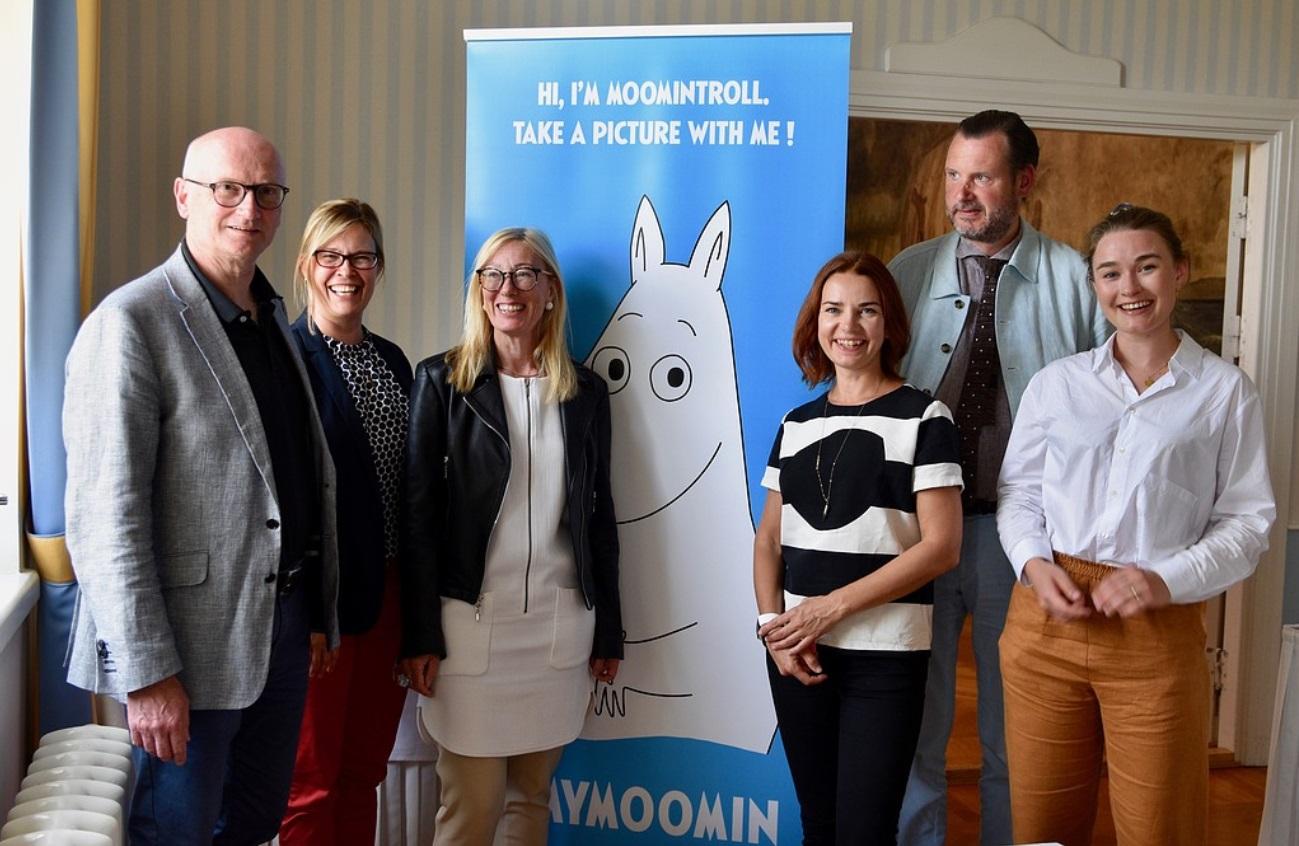 Flera personer står på rad vid ett muminplakat