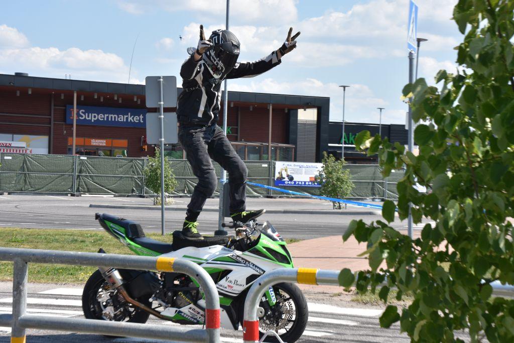 En man står på en motorcykel och visar segertecknet med sina händer.