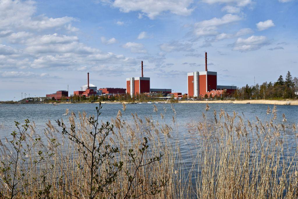 i förgrunden ser man vegetation och vatten. På andra sidan vattnet ser man siluetten av kärnkraftverket