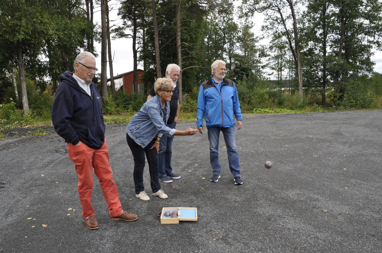 Fyra äldre personer spelar boule på en stor plan. Damen kastar sin kula.