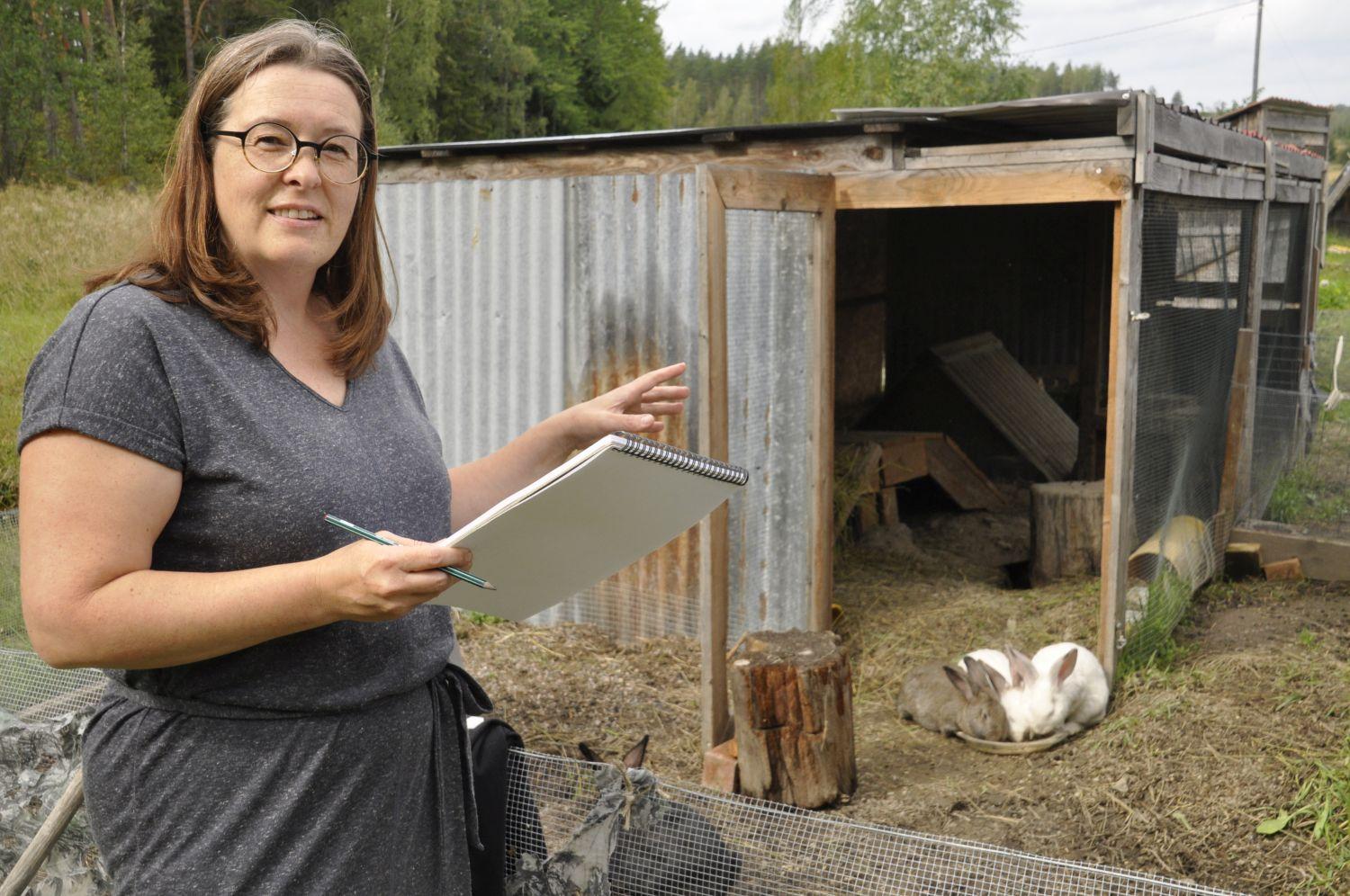Kvinna står med block och penna vid kanininhägnad.
