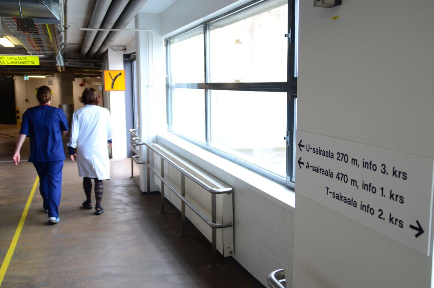 En tunnel där två sjuksköterskor går. På bilden syns också en skylt som pekar ut åt vilket håll och hur många meter man ska gå för att komma till A-, T- och U-sjukhusen.