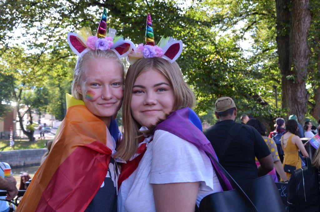 Två personer klädda i färggranna enhörningshorn kramas.