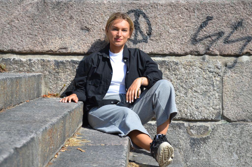 En ung kvinna sitter i en stentrappa och lutar sig mot en stenvägg som är täckt av med grafitti.