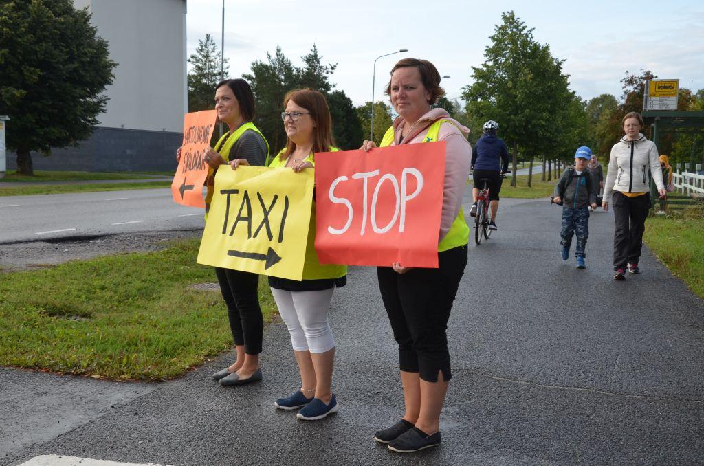 Tre kvinnor står och håller i färggranna skyltar med texterna "taxi" och "stop".