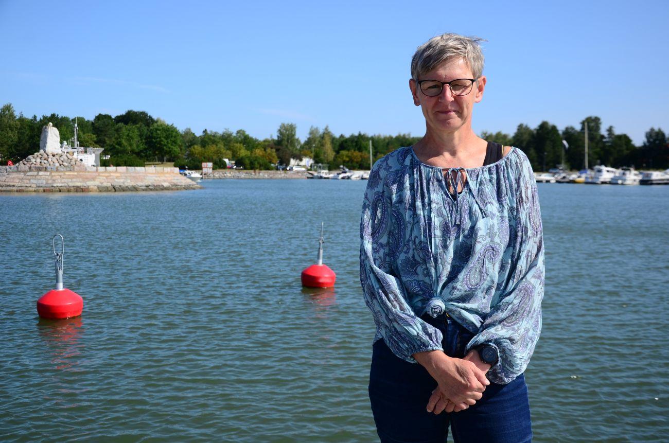 Kvinna står vid en strand, hav och bojar bakom henne