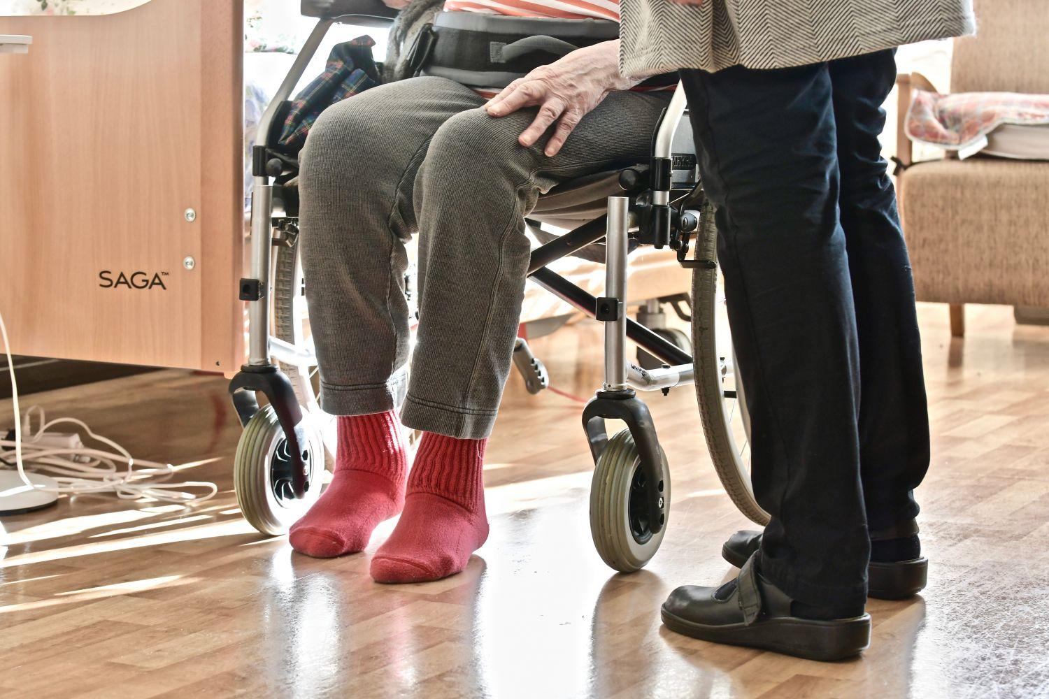 En äldre person som sitter på en rollator och enannan äldre person som står bredvid.