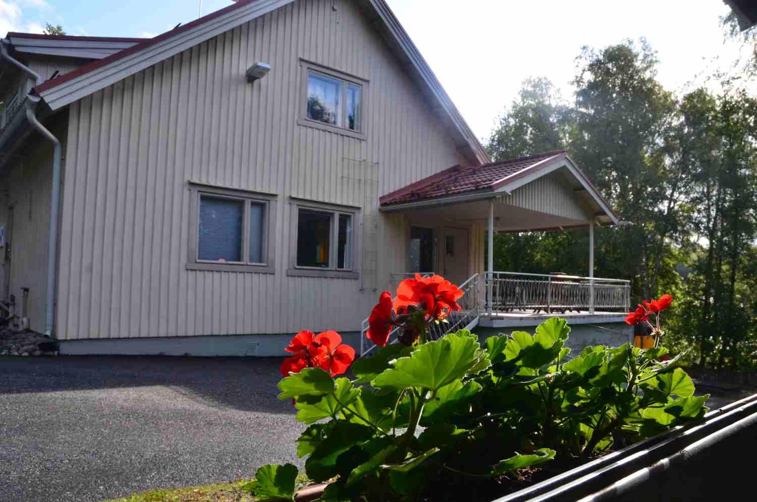Ett hus med röda pelargoner i förgrunden.
