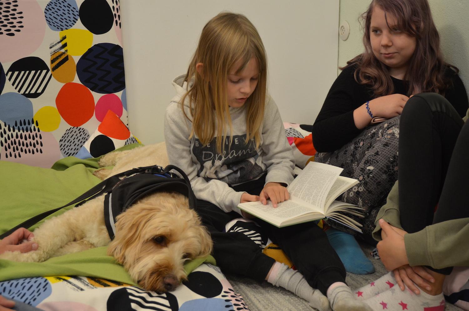 två flickor läser för en hund