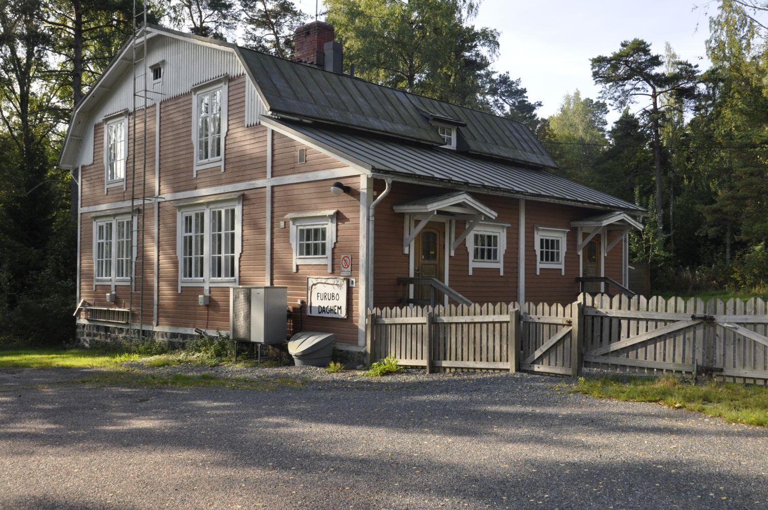 Träbyggnad i brunaktig färg, med gård omgiven av staket.