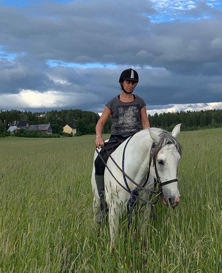 Dam sitter på en vit häst på en åker