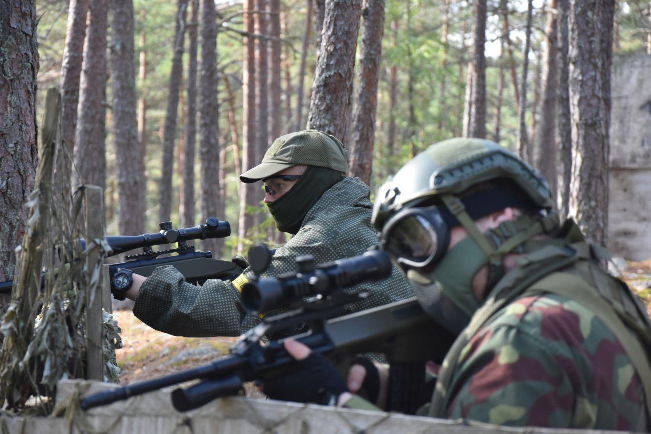Två män iklädda stridsutrustning och med airsoftvapen spanar efter motståndare.
