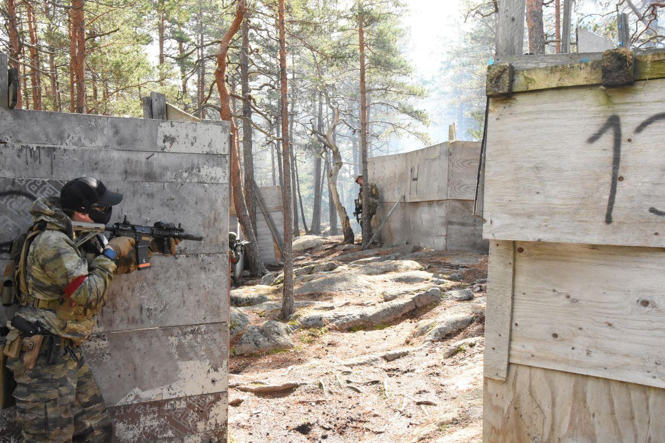 En man utklädd i airsoftutrutning väntar bakom en vägg före han framskrider på spelområdet.