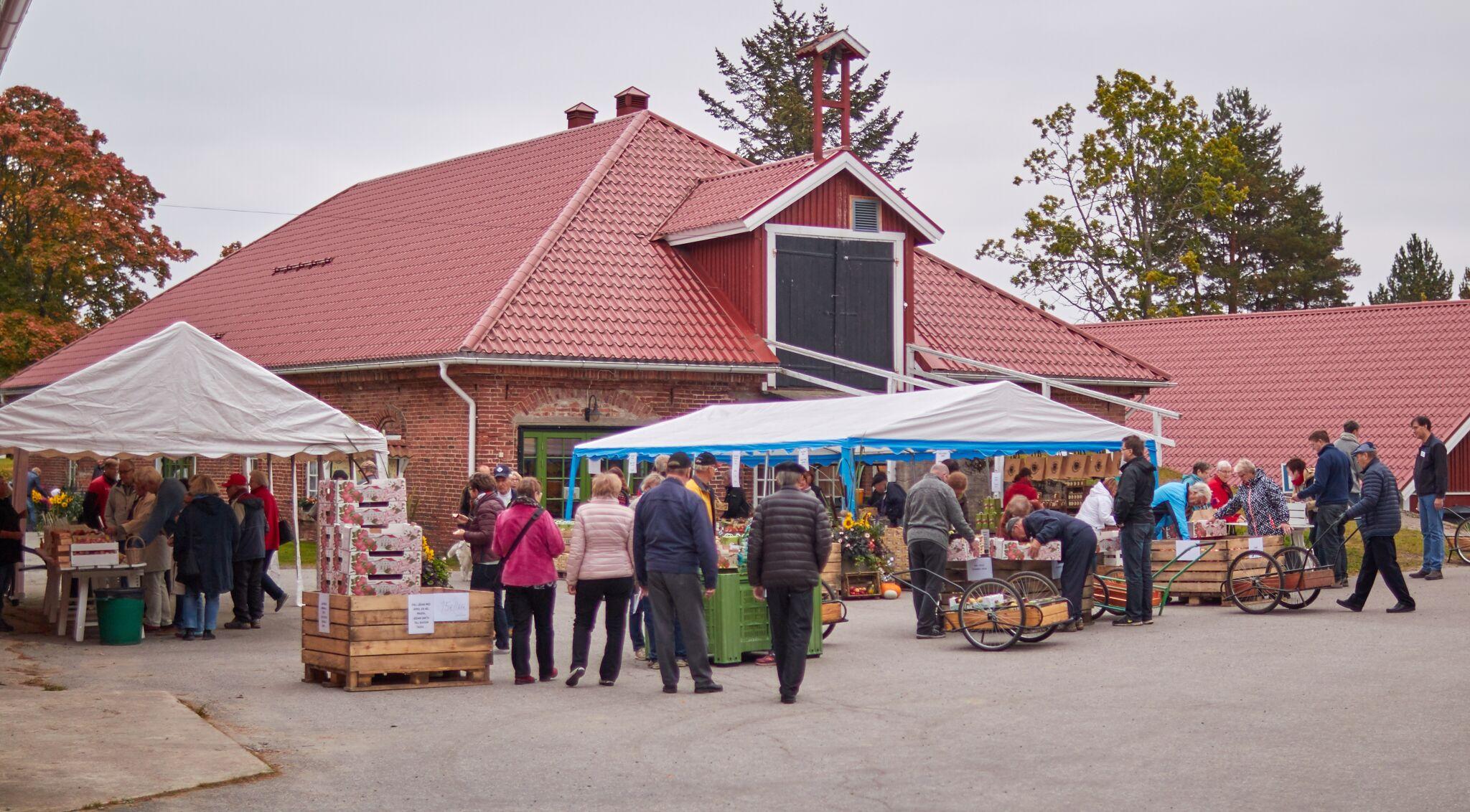 Marknadsstånd framför en byggnad. Mycket folk rör sig.