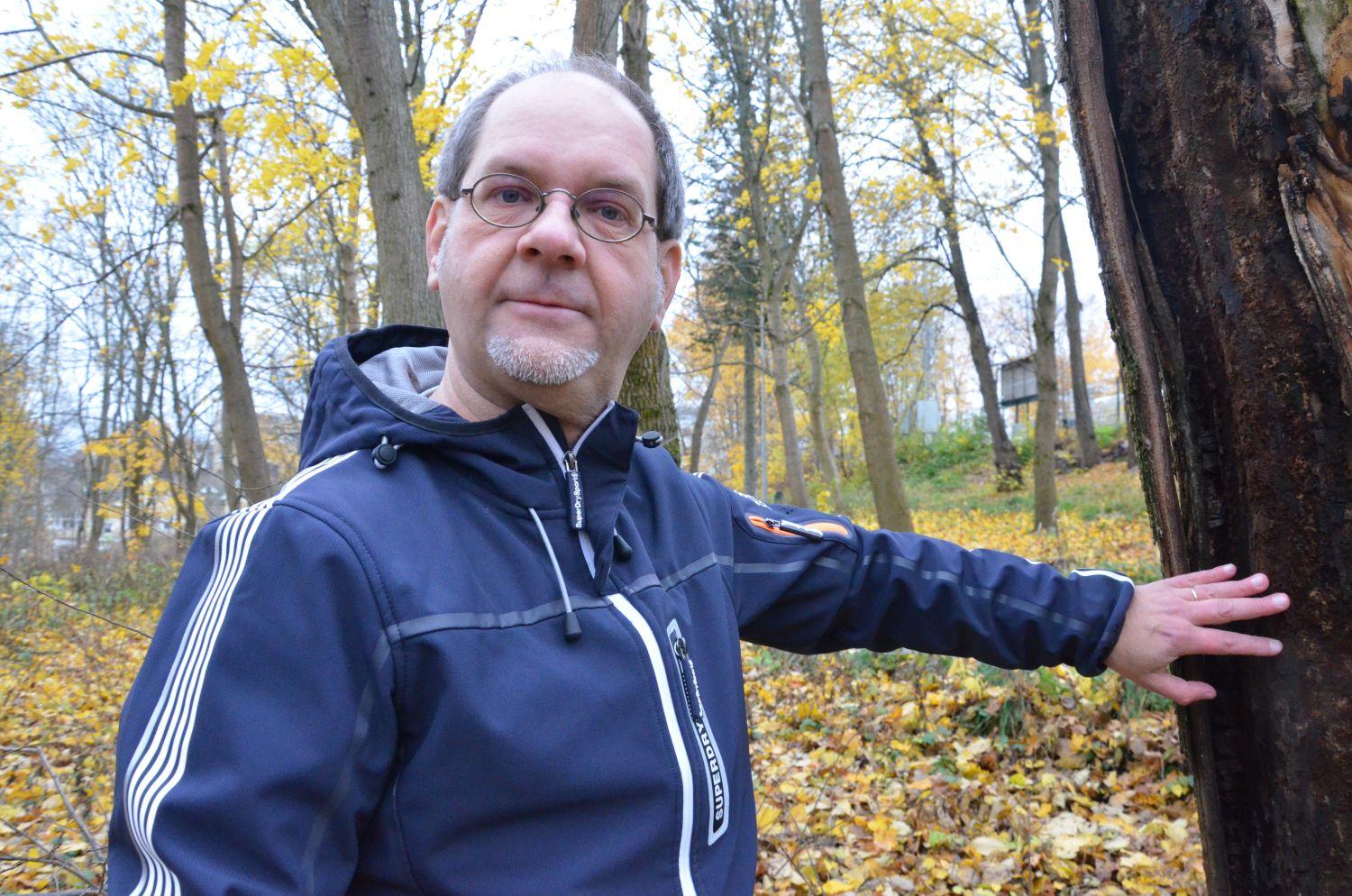 Man med glasögon håller sin hand på ett träd.