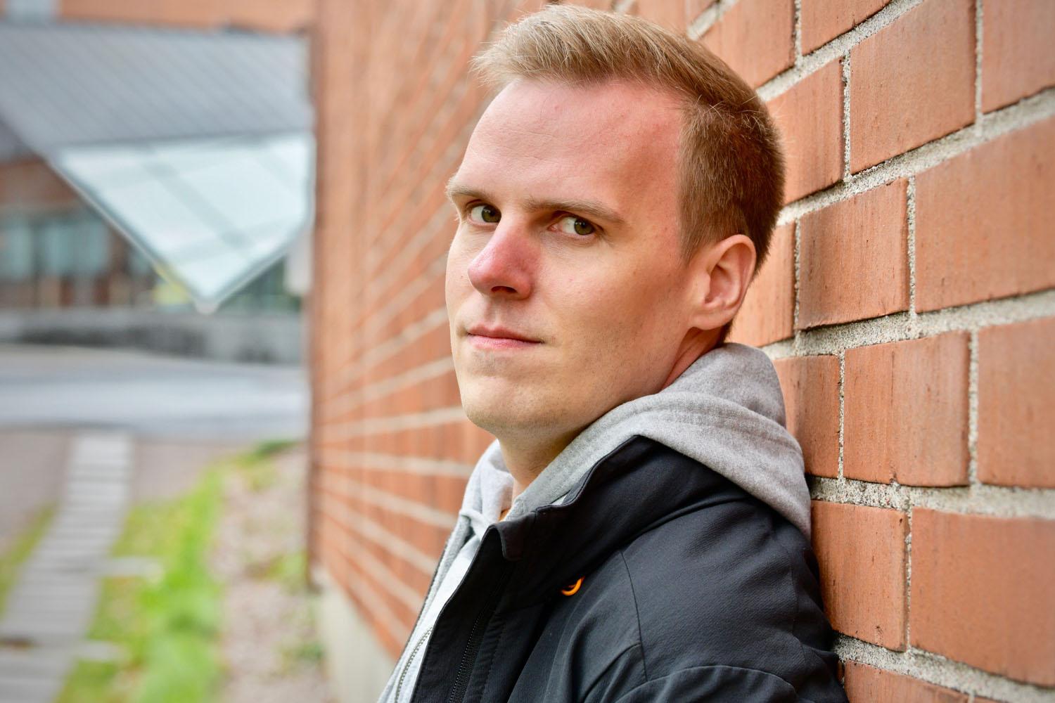 Närbild på man som lutar mot tegelvägg