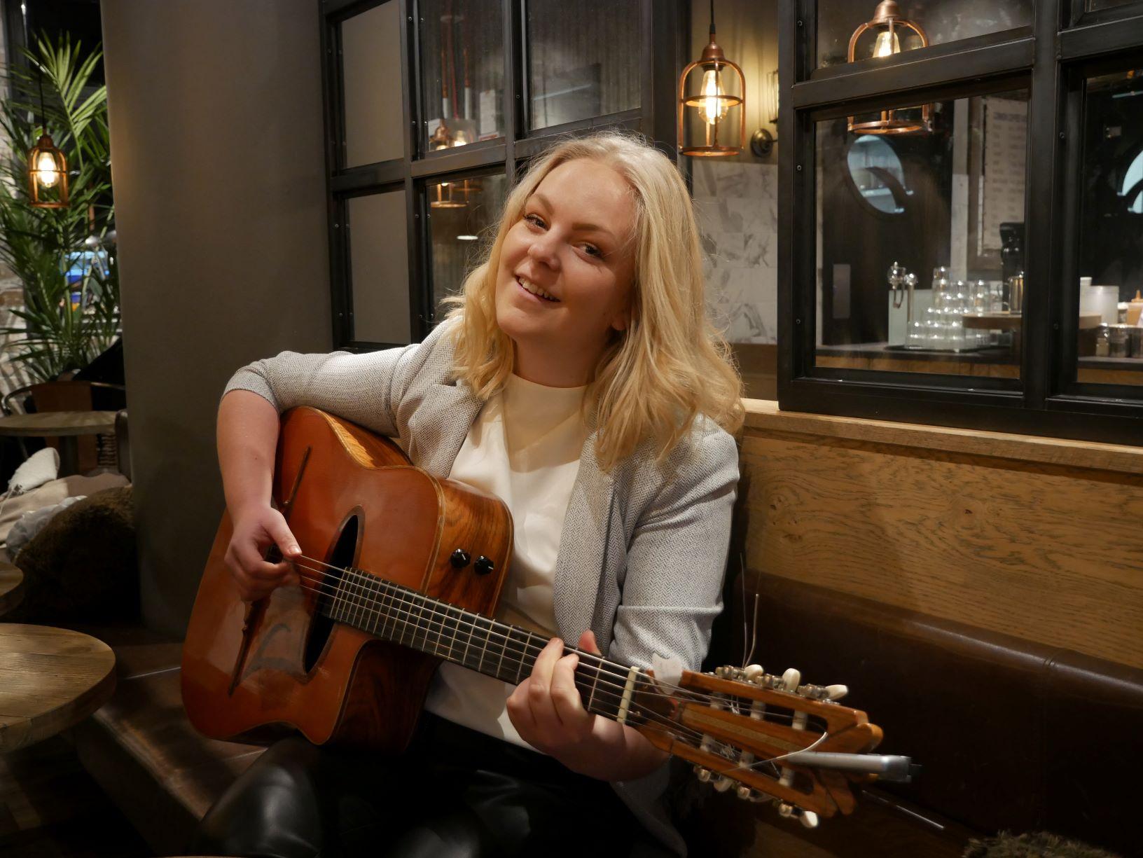 En kvinna sitter på café och spelar gitarr
