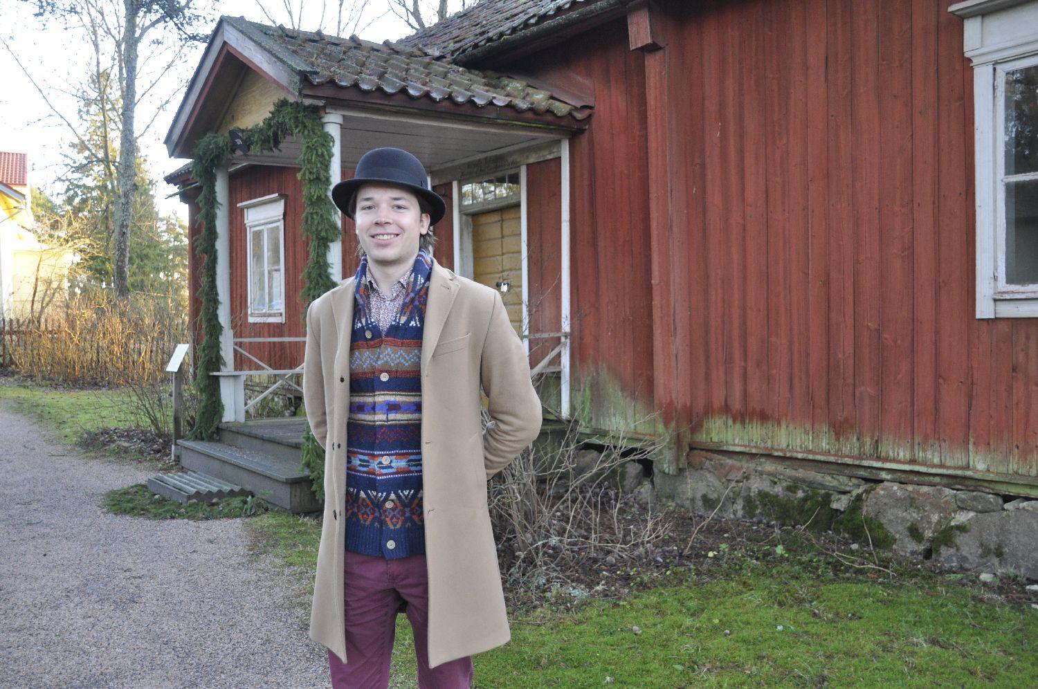 Ung man i hatt framför en gammal träbyggnad.