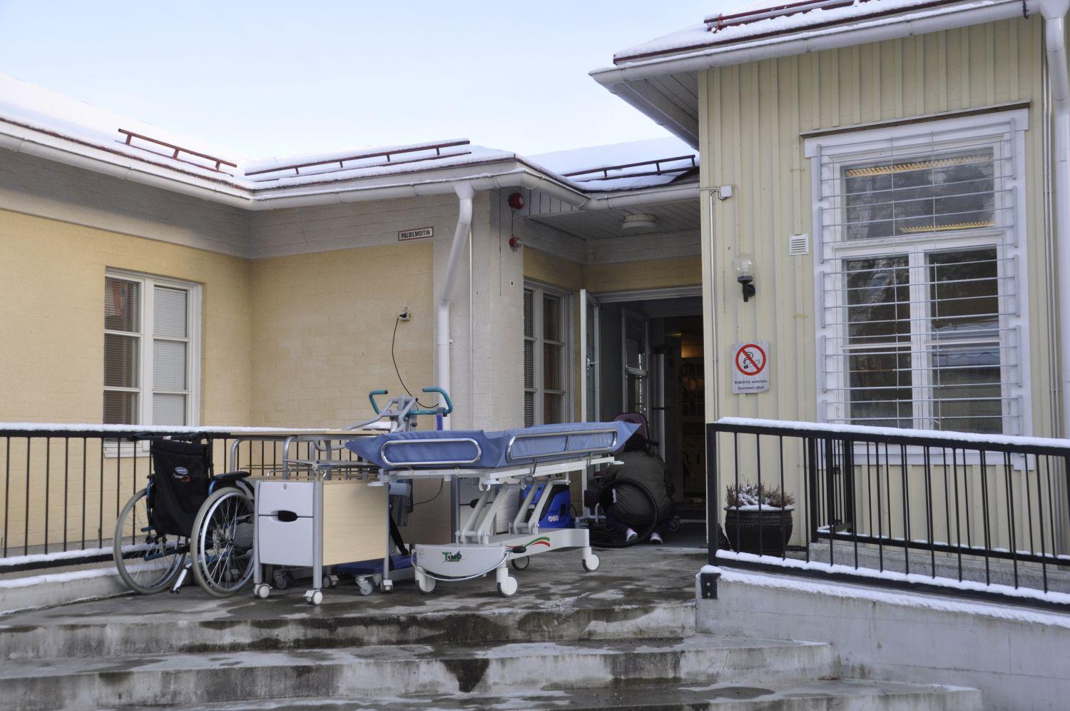 Trappan till en vårdfastighet. Här står en säng, en rullstol och lite andra grejer.