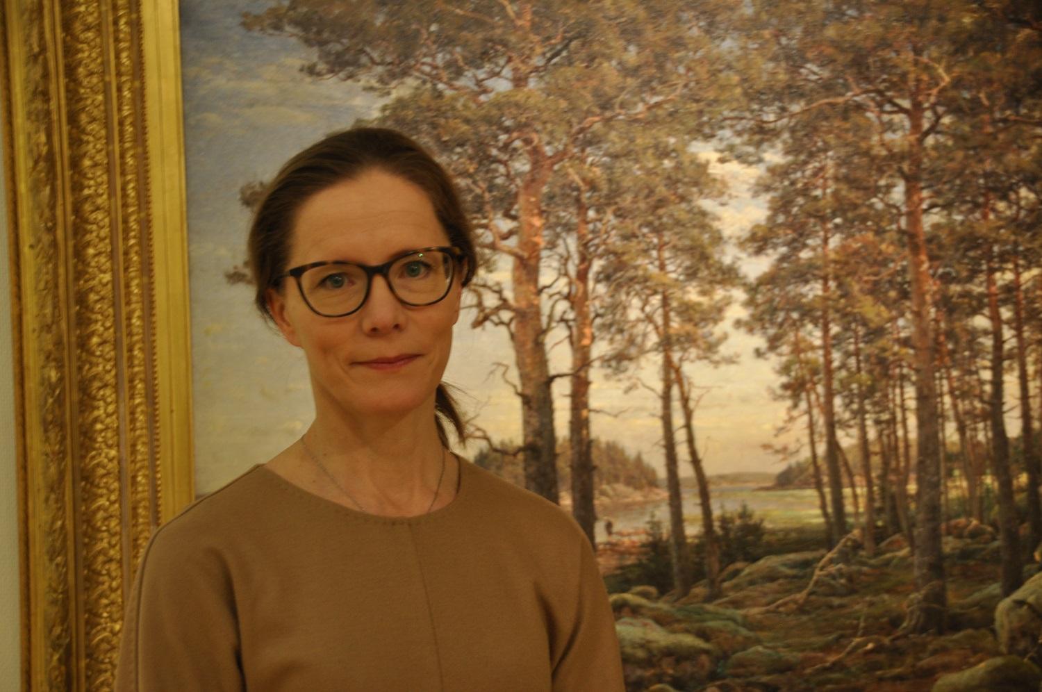 Kvinna står framför tavla med skog.