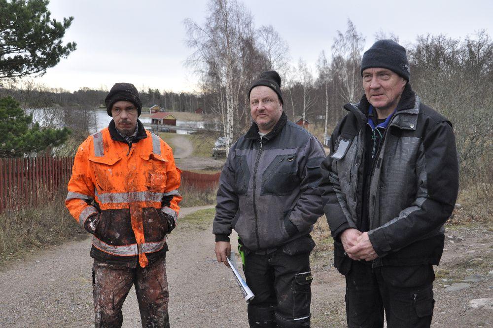 Tre män i arbetskläder utomhus.