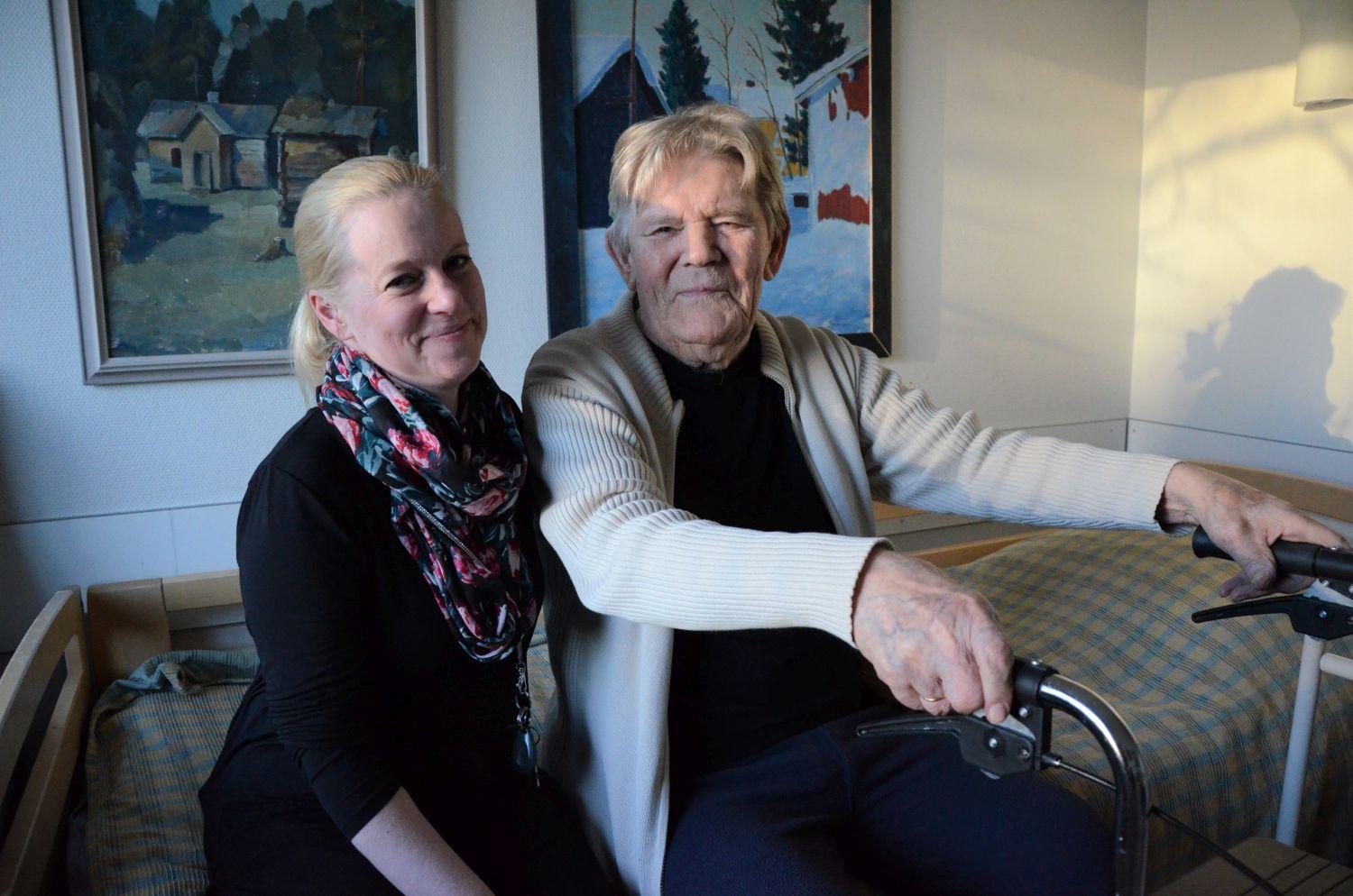 En kvinna och en äldre man sitter bredvid varandra på sängkanten.