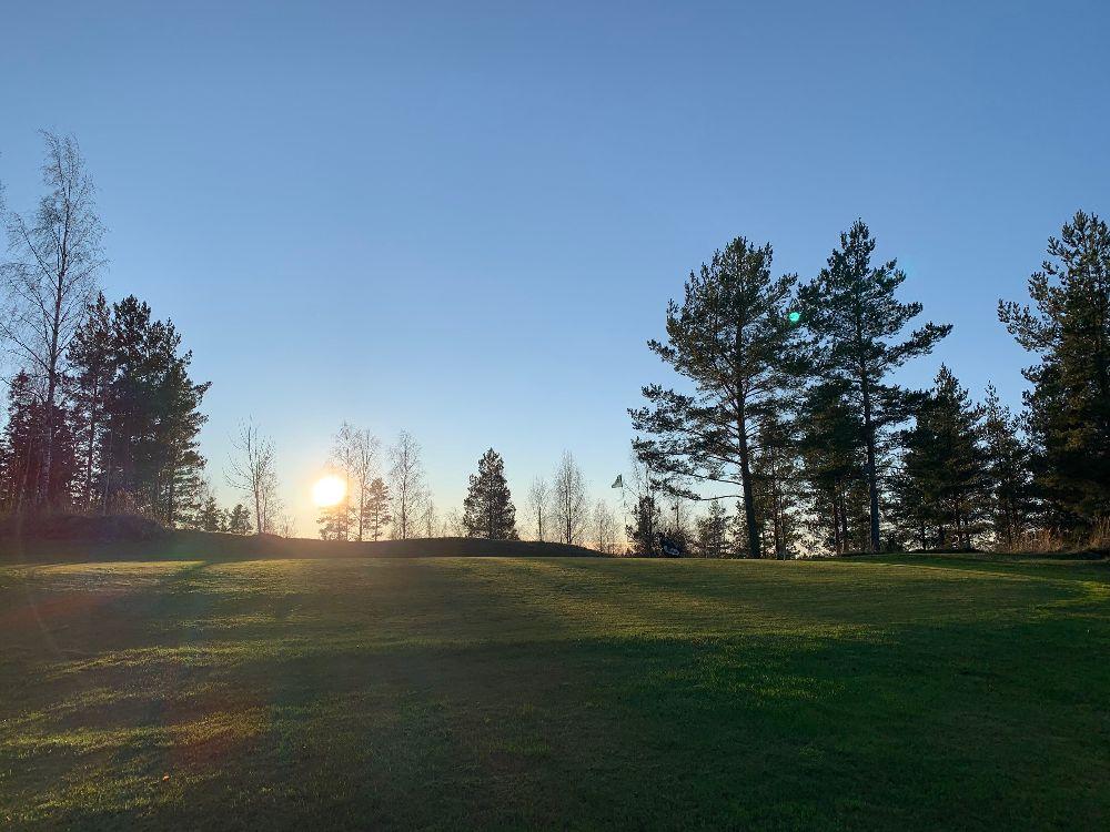 En grön backe av en golfbana, där solen tittar fram