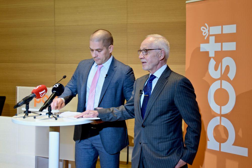 Två män vid mikrofoner och en Posti-banderoll