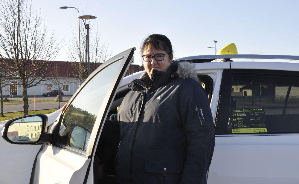 En dam står vid chaufförplatsen till en vit taxi.