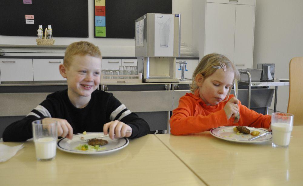 Två skolbarn sitter och äter i en skolmatsal.
