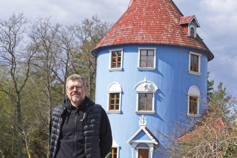 En vit man står framför ett muminhus