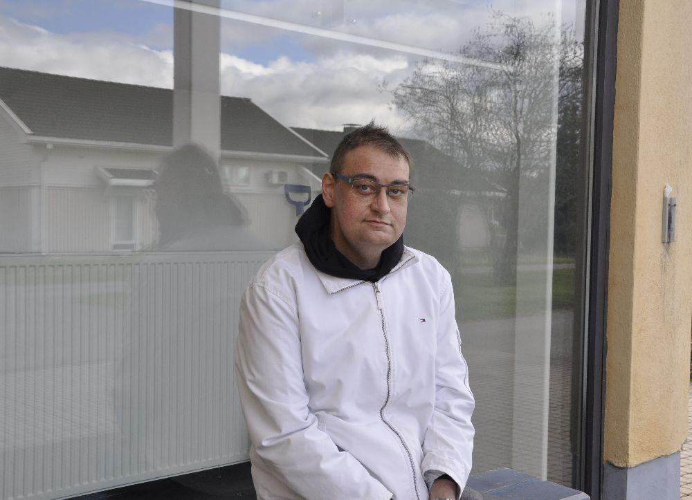 Man sitter på en bänk utomhus. I fönstret bakom honom speglas en byggnad