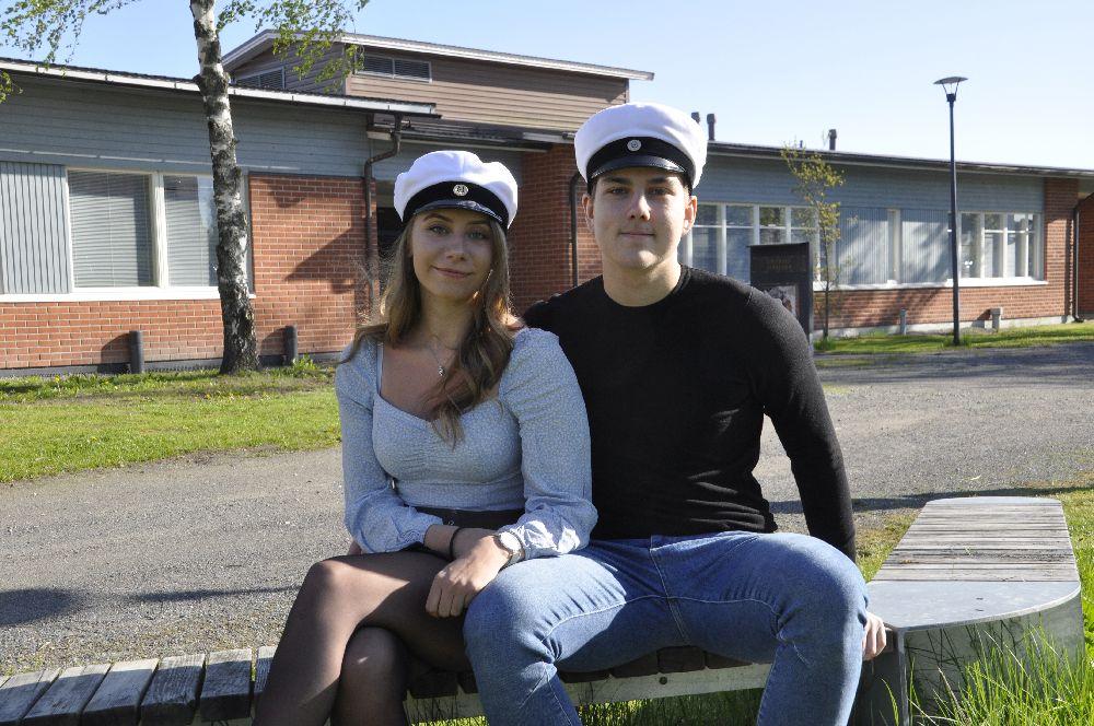 Ungdomar i studentmössor. Bakom syns en skolbyggnad