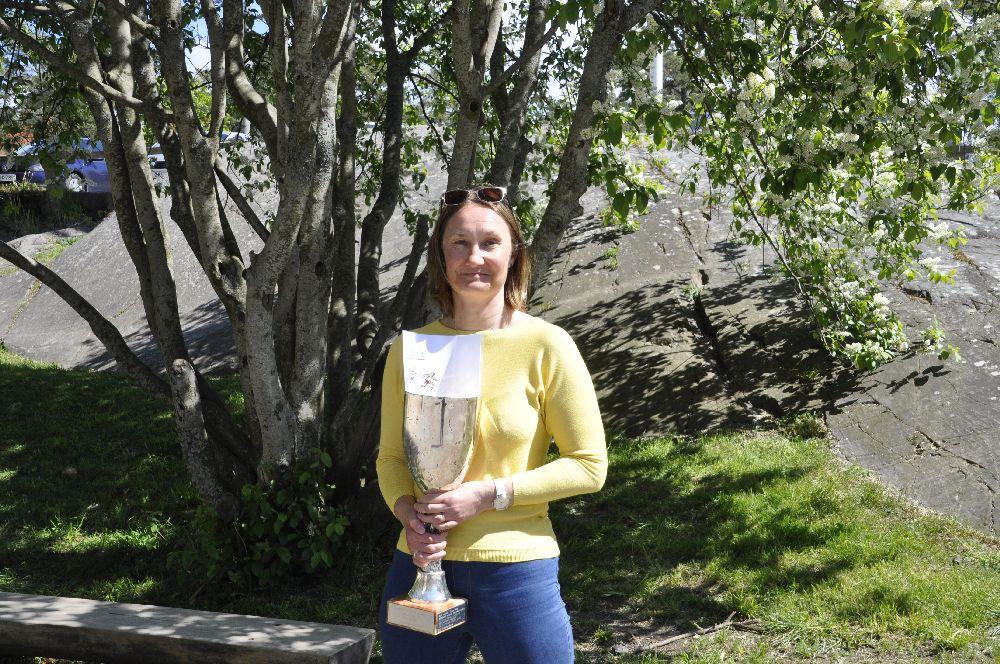 Glad dam med pokal i famnen vid ett träd på en skolgård