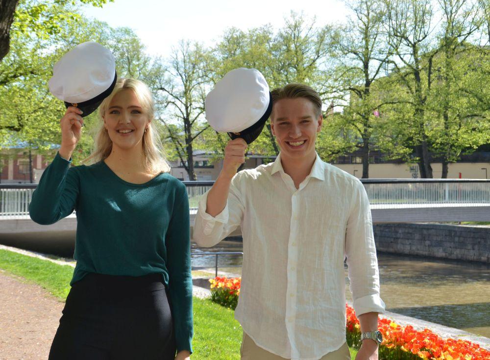 Ung kvinna och ung man med studentmössor i händerna.