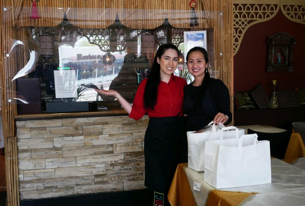två damer i indisk restaurang poserar framför hämtmatspåsar