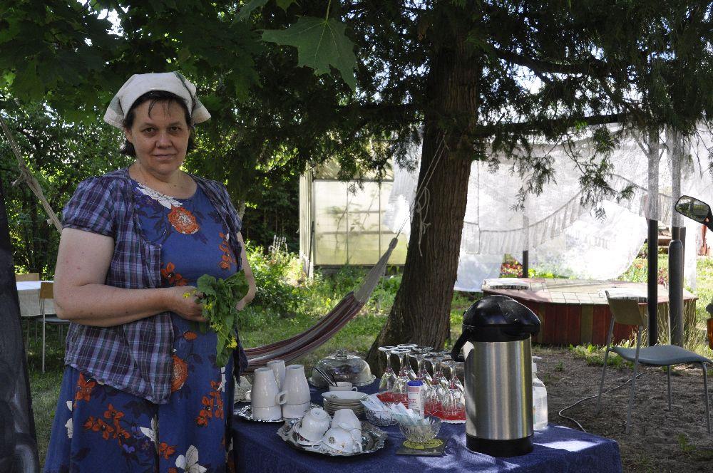 Cafévärdinna vid ett bord med kärl i en trädgård